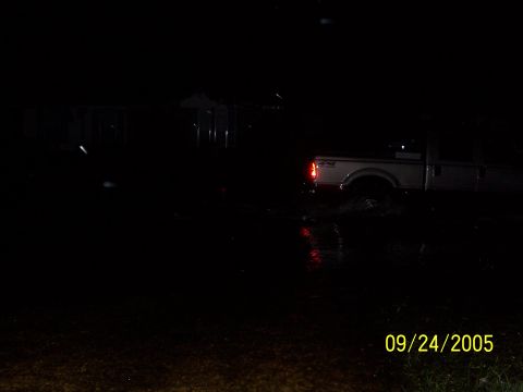 1992 Toyota Hilux - A white pickup truck navigates through a flooded area at night, with its taillights reflecting on the water's surface.