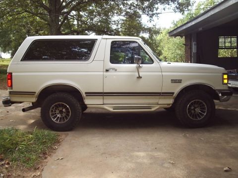 1978 Ford Bronco - This white Ford Bronco SUV, likely from the early 1990s, is parked on a concrete driveway next to a building.