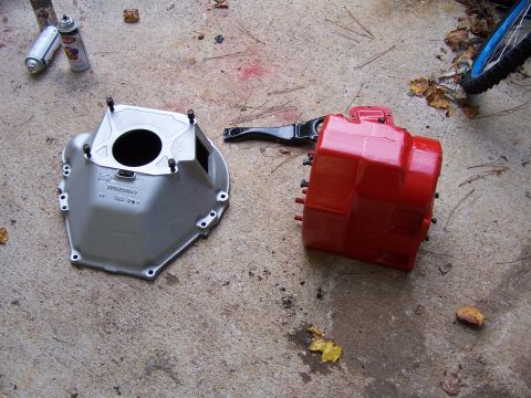 1979 Ford F-150 - Two automotive transmission parts, a bell housing and clutch fork, lie on a concrete surface next to spray cans.