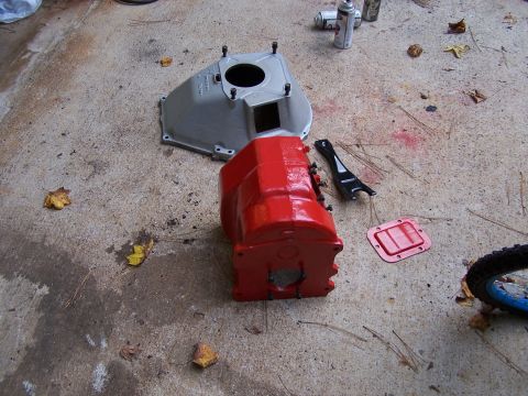 1979 Ford F-150 - Two painted transmission components, one red and one gray, lie on a concrete surface alongside a black tool and a red gasket.