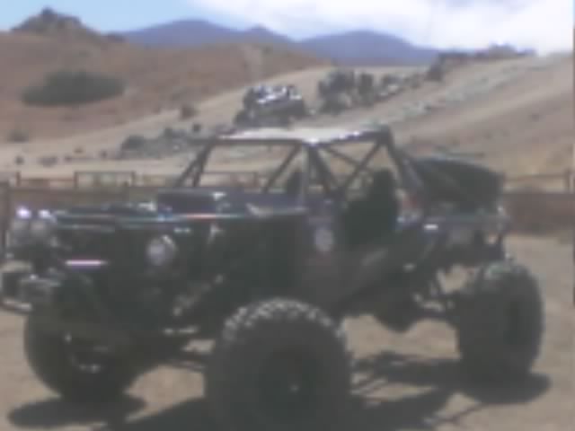 Black tube-chassis rock buggy with roll cage parked in a desert staging area