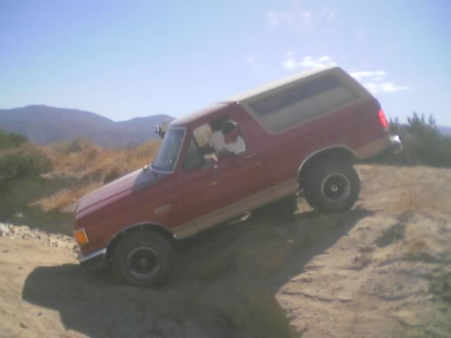Red Ford Bronco with tan lower body parked on a sandy desert slope at an angle