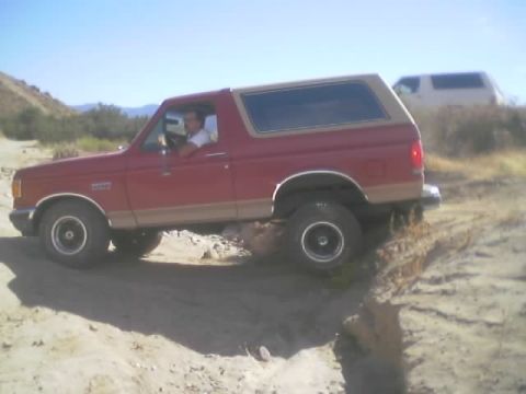 1990 Ford Bronco - red Ford Bronco with tan two-tone trim rests in a sandy desert wash with the driver seated behind the wheel.