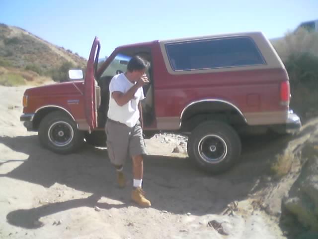 Man in white shirt stepping out of a red Ford Bronco parked in the desert