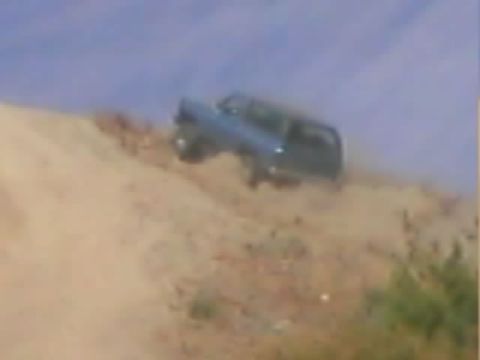 1990 Ford Bronco - blue-gray SUV descends a steep, eroded dirt hillside against a hazy blue sky.