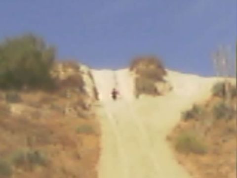 1990 Ford Bronco - small distant figure on a motorcycle ascends a steep sandy hill-climb trail flanked by dry brush.