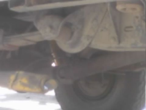 1990 Ford Bronco - close underbody view of a vehicle's suspension, axle, and tire with a yellow-painted component below.