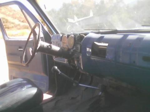 1990 Ford Bronco - interior of a vintage truck showing a steering wheel, partly stripped teal dashboard, and floor shifter.