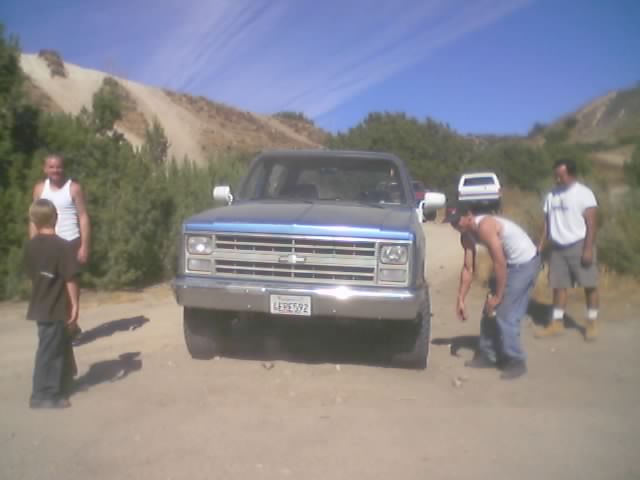 Blue and silver Chevrolet square-body truck with people on a dirt road