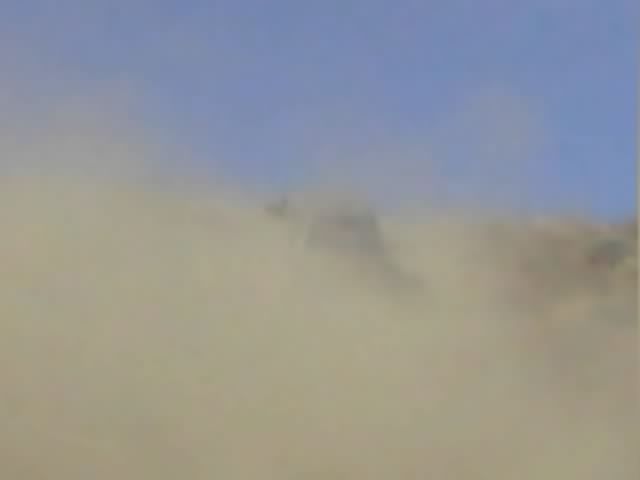 Blurry hillside obscured by a heavy dust cloud under blue sky