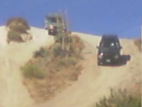 1990 Ford Bronco - Two off-road vehicles sit along a steep sandy hillside trail under a clear blue sky.