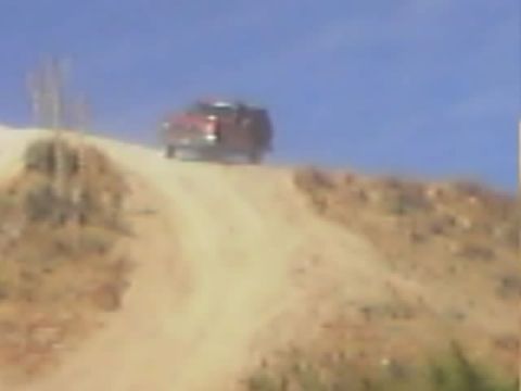 1990 Ford Bronco - red SUV crests the top of a sandy hill on a worn dirt trail beneath a clear blue sky.