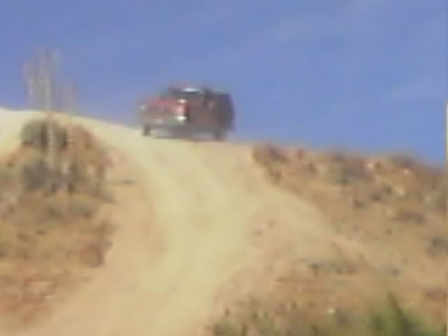 Red SUV cresting a sandy hill on a dirt trail under blue sky