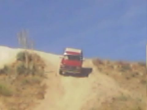 1990 Ford Bronco - red-and-white truck descends a steep sandy hill trail surrounded by dry desert brush.
