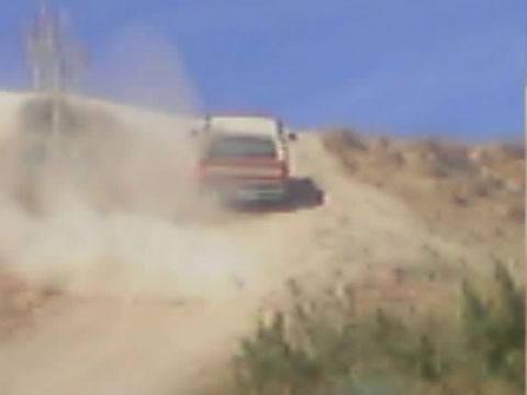 1990 Ford Bronco - red-and-white truck kicks up dust as it drives along a steep sandy hill trail.