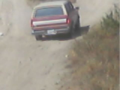 1990 Ford Bronco - rear of a maroon SUV with a white roof and full-width taillight panel on a dusty dirt trail.