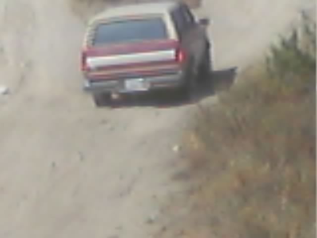 Rear view of a maroon SUV with white top on a dirt off-road trail