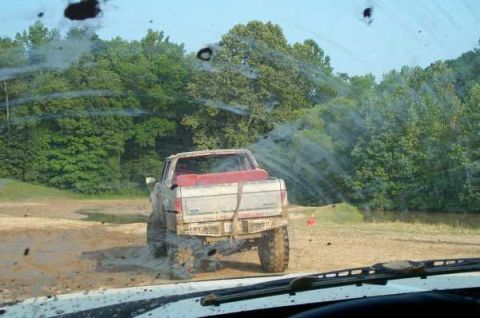 1988 Ford Bronco - Pickup truck stuck in mud, seen from inside another vehicle's windshield.