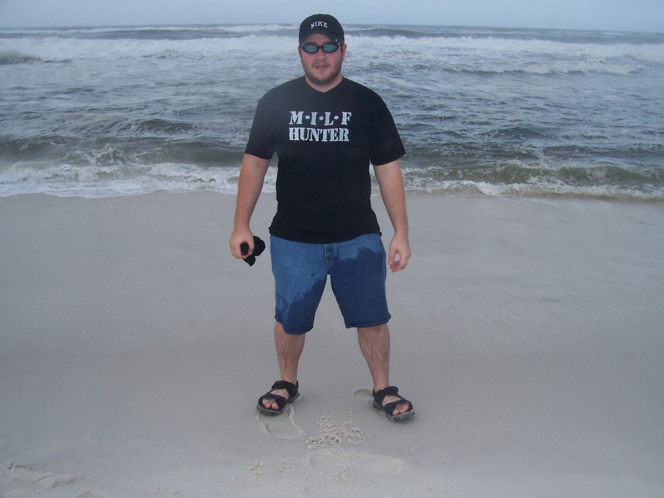 Man in black t-shirt and denim shorts on a sandy beach with waves in the background