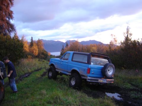 1988 Ford Bronco - Blue 1988 Ford Bronco navigating a muddy off-road trail during sunset.