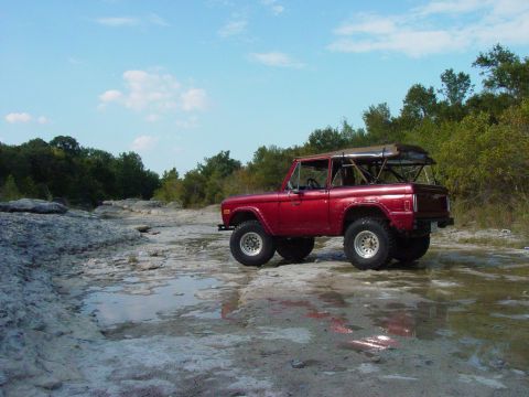 1977 Ford Bronco - A red 1977 Ford Bronco sits off-road in a dry creek bed under a blue sky.