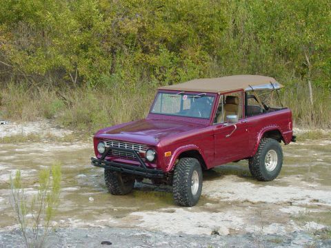 1977 Ford Bronco - This 1977 Ford Bronco features a tan soft top and off-road tires, parked in an outdoor setting.