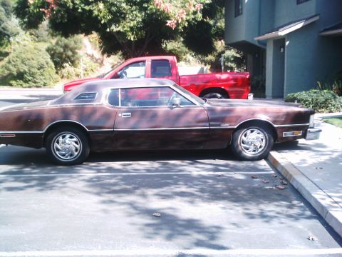 1986 Ford Bronco - Side profile of a 1970s Ford Thunderbird two-door hardtop in weathered brown paint with a faded vinyl roof, opera windows and chrome five-s…