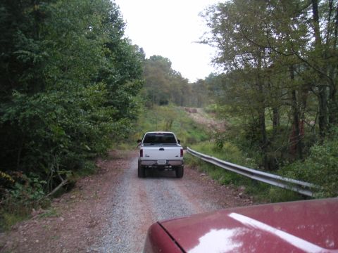 1994 Ford Bronco - Two vehicles on a gravel road surrounded by trees. The lead vehicle is a white pickup truck.