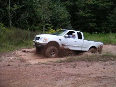 1994 Ford Bronco - A white pickup truck navigates a muddy trail, kicking up dirt as it goes.