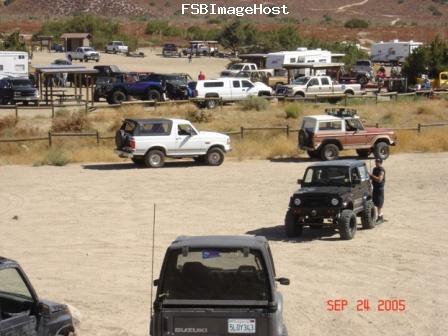 1988 Ford Bronco - Several off-road vehicles are parked in a dusty lot with RVs and campers in the background.