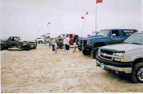 1977 Ford F-150 - A group of trucks and people gathered on a sandy beach, possibly for an off-road event.