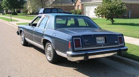 1985 Ford Crown Victoria LTD - Rear view of a blue 1985 Ford Crown Victoria LTD sedan parked on a suburban street, showing its distinctive taillights and chrome bumper.