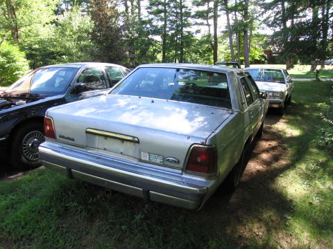 1991 Ford LTD Crown Victoria - A silver 1990 Ford Crown Victoria sedan is parked outdoors next to other vehicles.