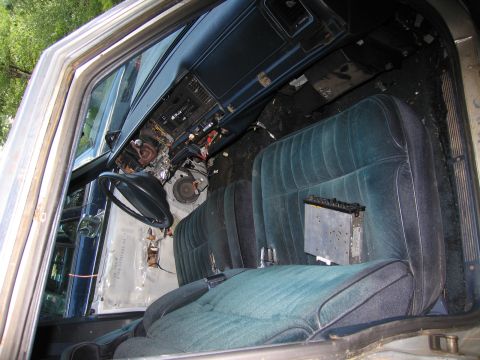 1991 Ford LTD Crown Victoria - The interior of a car shows teal velour seats and a heavily damaged dashboard, suggesting it is in disrepair.