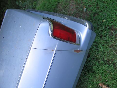 1991 Ford LTD Crown Victoria - The rear quarter panel of a silver car shows a red taillight and chrome trim, with visible rust spots.