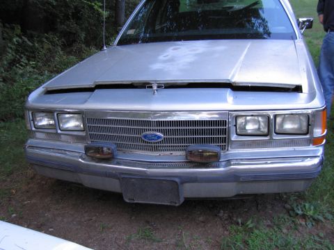 1991 Ford LTD Crown Victoria - Close-up head-on view of the front end of a silver Ford LTD Crown Victoria, showing the horizontal-bar grille with Ford blue oval, quad rec…