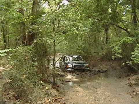 1986 Ford Bronco - Ford Bronco navigating a difficult muddy path through a wooded area.