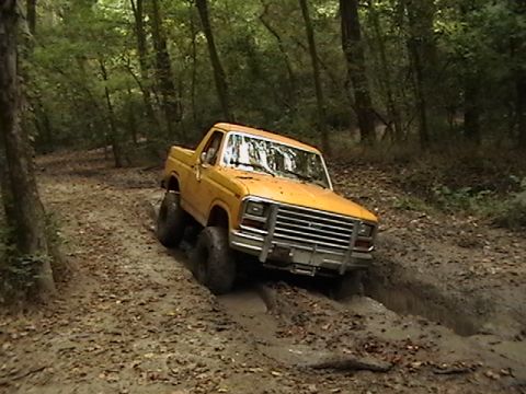 1986 Ford Bronco - This yellow pickup truck is off-roading through a muddy path in the woods.
