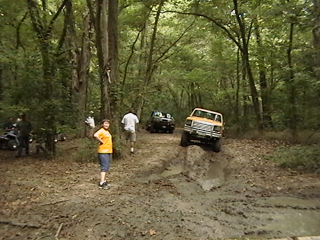 1986 Ford Bronco navigating a muddy trail with other vehicles in the background