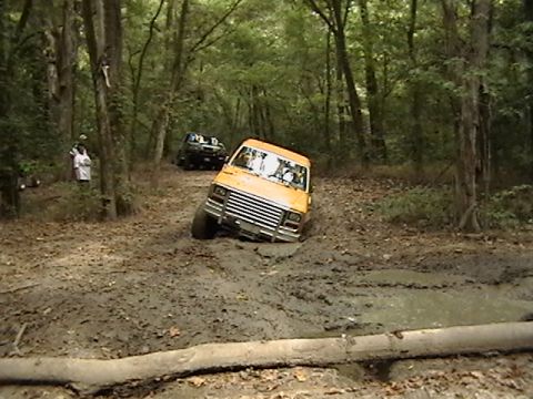1986 Ford Bronco - Two off-road vehicles navigate a challenging muddy path through a dense forest.
