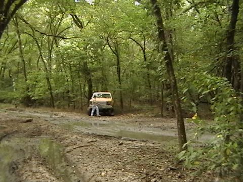1986 Ford Bronco - A yellow SUV navigates a muddy, wooded trail.