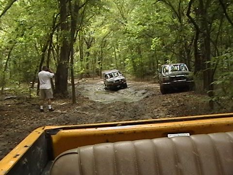 1986 Ford Bronco - Off-roading adventure in a wooded area with muddy terrain.