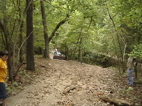1986 Ford Bronco - A Ford Bronco navigates a wooded trail with people nearby.
