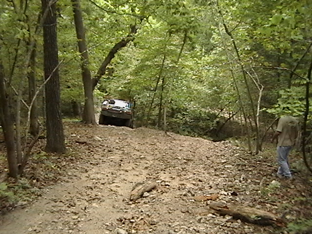 Off-road vehicle climbing a dirt path in a wooded area
