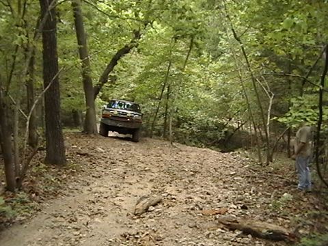 1986 Ford Bronco - Ford Bronco navigates a wooded trail, kicking up dust on the path.