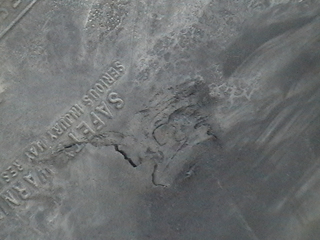 Cracked gray plastic panel with embossed safety warning text, showing damage near center