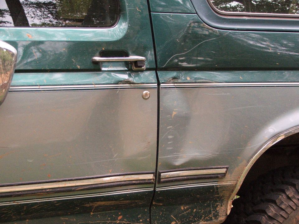 Green and silver SUV door with dents and scratches, chrome handle, visible tire tread
