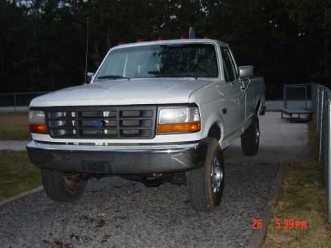 1995 Dodge 1500 - A white Ford F-Series truck is parked on a gravel surface with trees in the background.