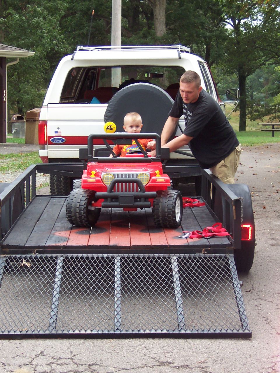 1989 Ford Bronco parked next to a trailer carrying a red toy Jeep with a baby inside