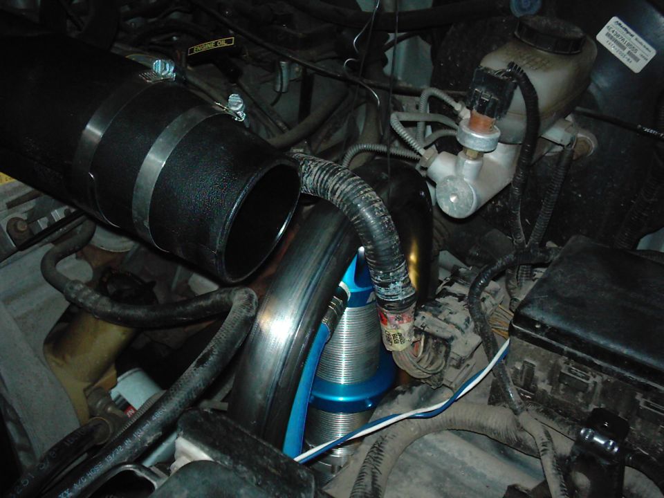 Close-up of engine bay showing large intake tube, blue coilover shock, and brake fluid reservoir